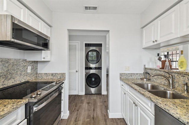 kitchen featuring stainless steel appliances, stacked washer / dryer, white cabinets, and sink