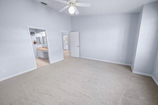 unfurnished bedroom with ensuite bath, light colored carpet, ceiling fan, and a high ceiling