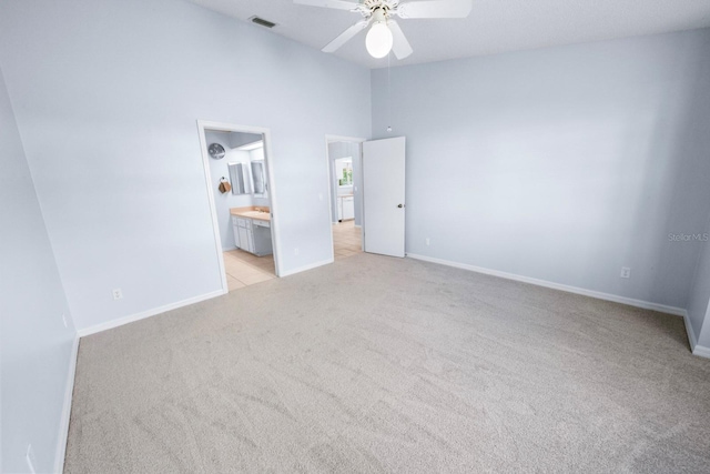 unfurnished bedroom with a towering ceiling, connected bathroom, light colored carpet, and ceiling fan