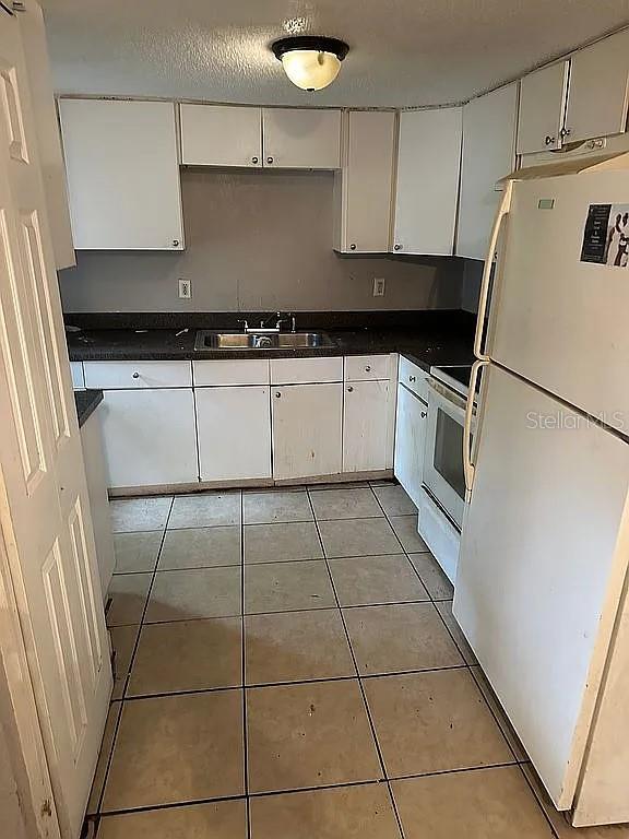 kitchen with light tile patterned floors, sink, white cabinets, and white appliances