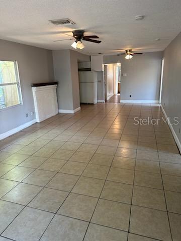 unfurnished living room featuring ceiling fan, light tile patterned floors, and a textured ceiling