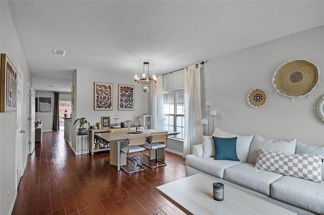 living room featuring dark wood-type flooring, a textured ceiling, an inviting chandelier, and a healthy amount of sunlight