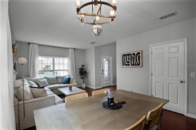 dining area featuring dark hardwood / wood-style flooring, a textured ceiling, and a notable chandelier