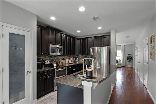 kitchen with decorative backsplash, sink, light hardwood / wood-style flooring, an island with sink, and stainless steel appliances