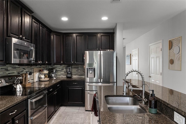 kitchen with light tile patterned floors, stainless steel appliances, decorative backsplash, dark stone counters, and sink