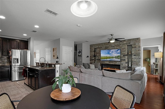 dining space featuring light hardwood / wood-style floors, a stone fireplace, ceiling fan, a textured ceiling, and sink