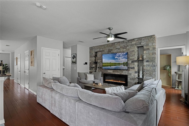 living room with ceiling fan, dark hardwood / wood-style floors, a stone fireplace, and a textured ceiling