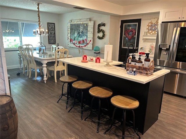 kitchen with pendant lighting, a breakfast bar, white cabinetry, an island with sink, and stainless steel fridge with ice dispenser