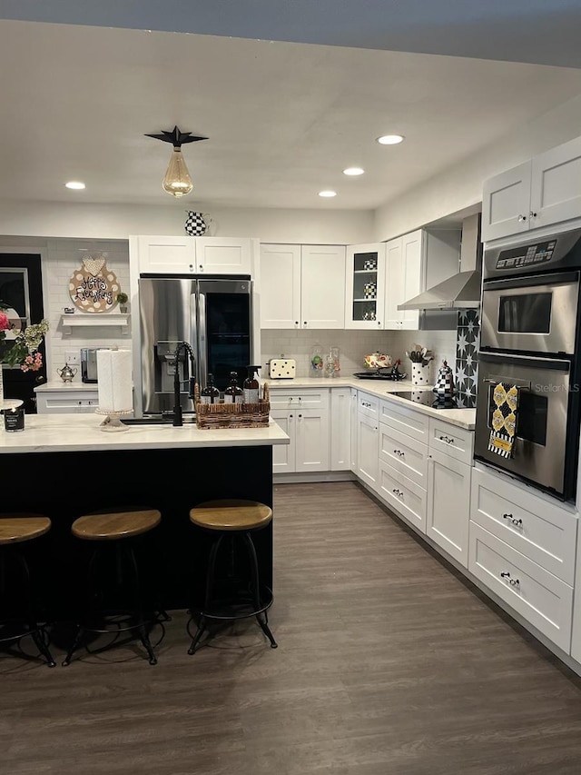 kitchen with white cabinetry, wall chimney range hood, a kitchen bar, and appliances with stainless steel finishes