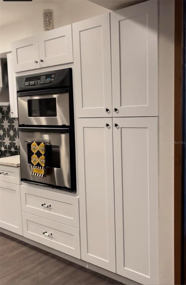 kitchen with white cabinetry, stainless steel double oven, dark hardwood / wood-style flooring, and backsplash