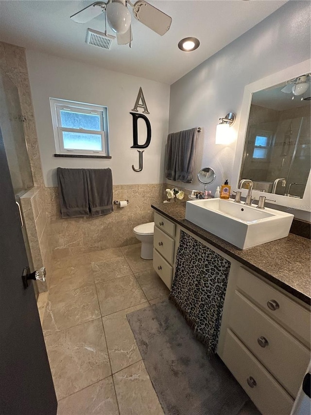 bathroom with tile walls, vanity, ceiling fan, walk in shower, and toilet