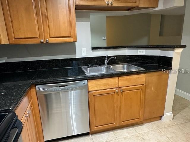 kitchen with dishwasher, light tile patterned floors, stove, sink, and dark stone counters