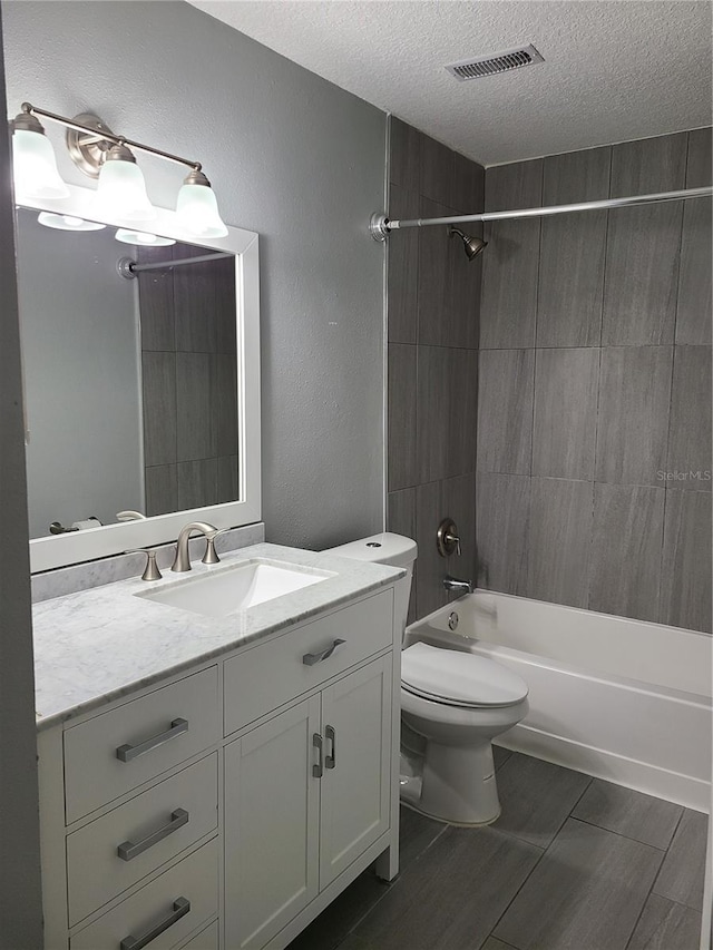 full bathroom with vanity, toilet, tiled shower / bath, and a textured ceiling