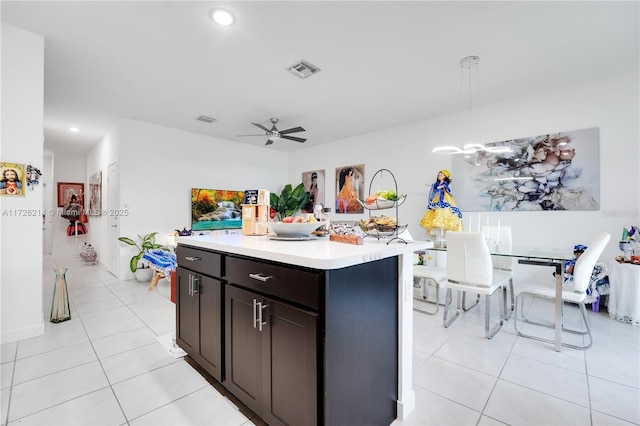 kitchen featuring ceiling fan, pendant lighting, dark brown cabinetry, an island with sink, and light tile patterned floors