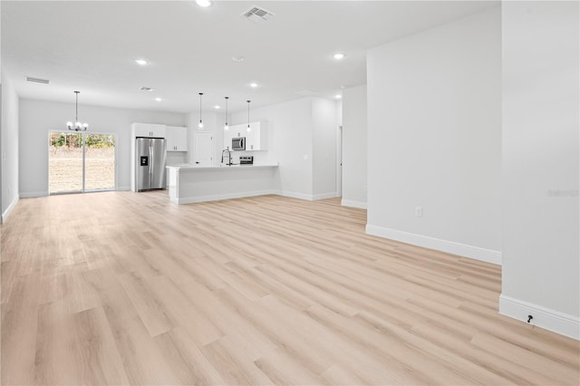 unfurnished living room with a notable chandelier, sink, and light wood-type flooring