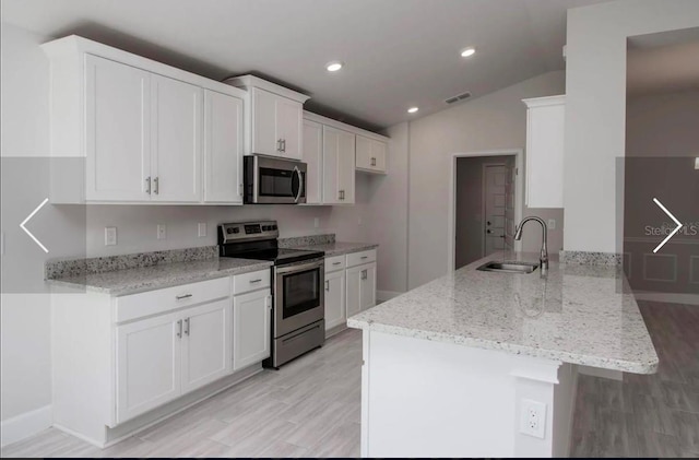 kitchen with white cabinetry, appliances with stainless steel finishes, kitchen peninsula, and vaulted ceiling