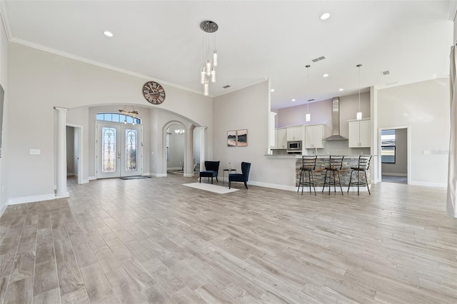 unfurnished living room featuring decorative columns, crown molding, a towering ceiling, and light wood-type flooring