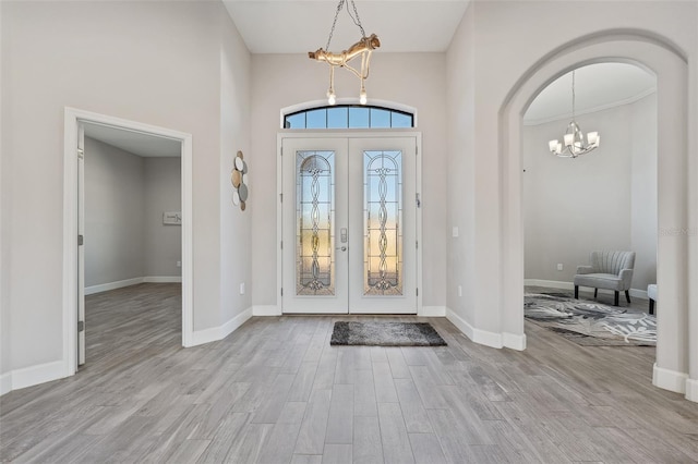 entryway featuring a notable chandelier, a towering ceiling, light hardwood / wood-style flooring, and french doors