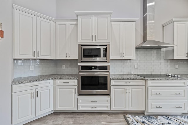 kitchen featuring white cabinetry, appliances with stainless steel finishes, backsplash, and wall chimney range hood