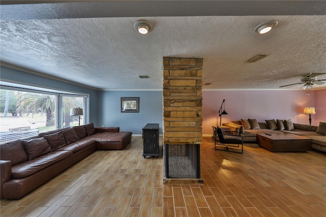 living room featuring ceiling fan, ornamental molding, and a stone fireplace