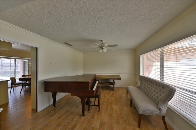 game room with ceiling fan, plenty of natural light, ornamental molding, and a textured ceiling