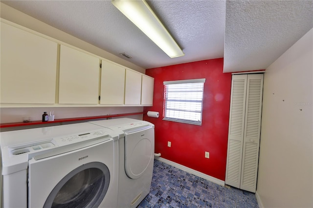 laundry area with independent washer and dryer, a textured ceiling, and cabinets