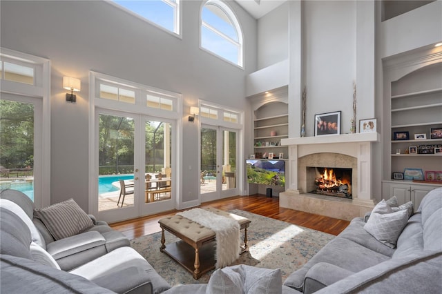 living room featuring hardwood / wood-style flooring, a high ceiling, a premium fireplace, french doors, and built in shelves