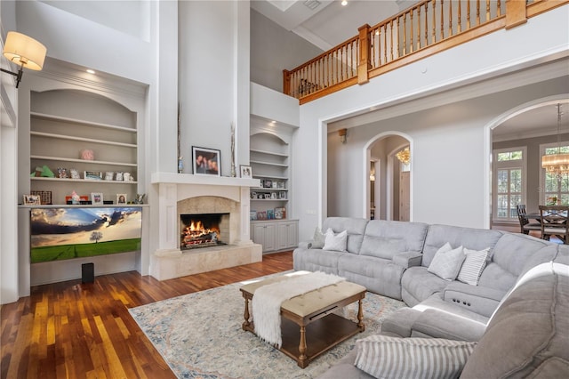 living room featuring a high ceiling, built in shelves, dark hardwood / wood-style flooring, and crown molding