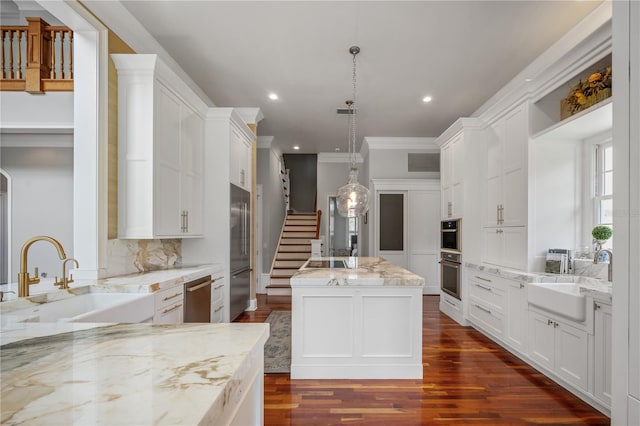 kitchen featuring light stone countertops, pendant lighting, a center island, white cabinetry, and sink