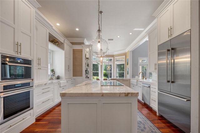 kitchen with white cabinets, a kitchen island, decorative light fixtures, stainless steel appliances, and light stone counters