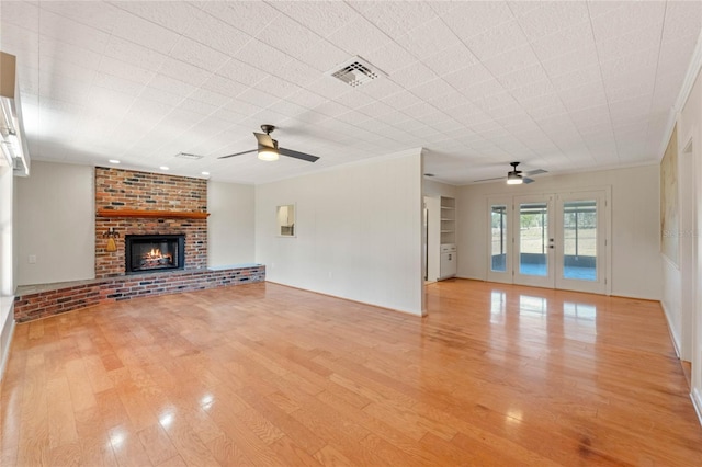 unfurnished living room featuring crown molding, a brick fireplace, light wood-type flooring, and french doors