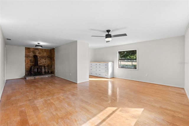 unfurnished living room featuring ceiling fan, light hardwood / wood-style flooring, and a wood stove