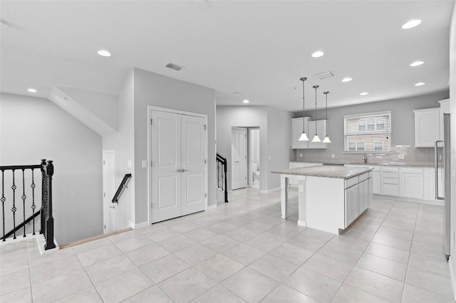 kitchen with light stone countertops, white cabinets, a kitchen island, decorative light fixtures, and backsplash