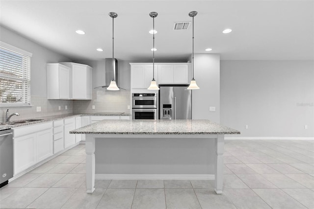 kitchen with a kitchen island, wall chimney range hood, stainless steel appliances, sink, and hanging light fixtures