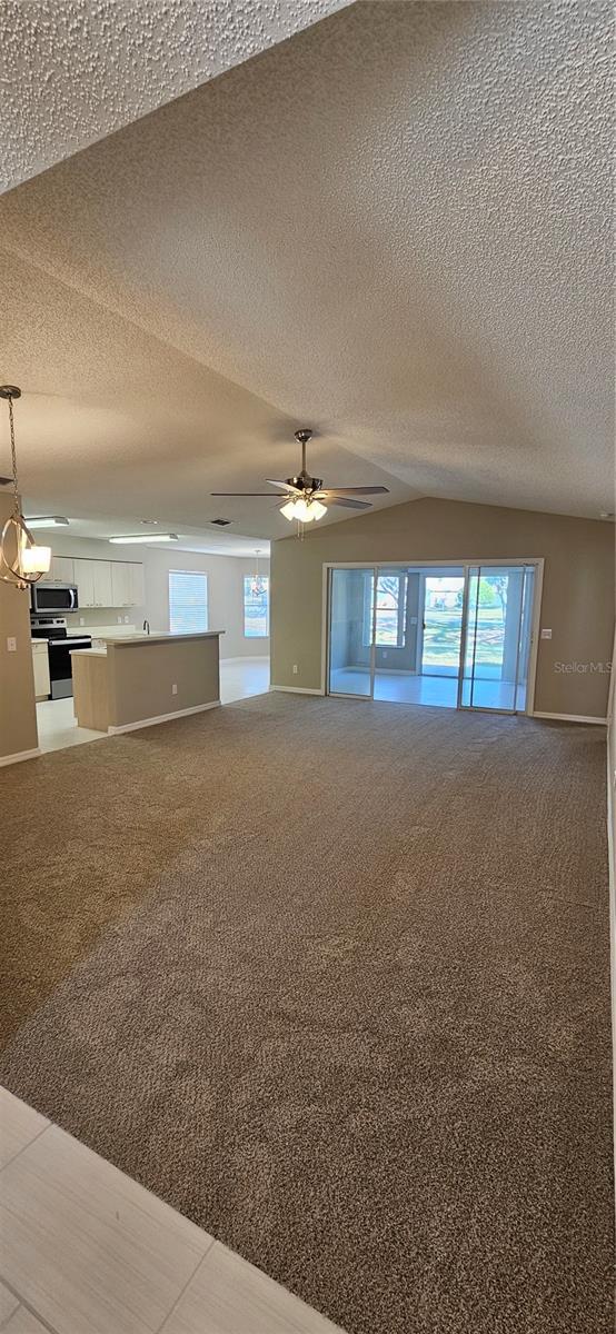 carpeted empty room with ceiling fan, a textured ceiling, and vaulted ceiling