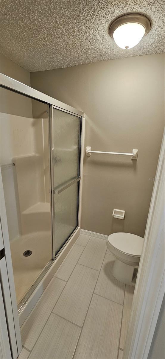 bathroom with toilet, a shower with shower door, and a textured ceiling