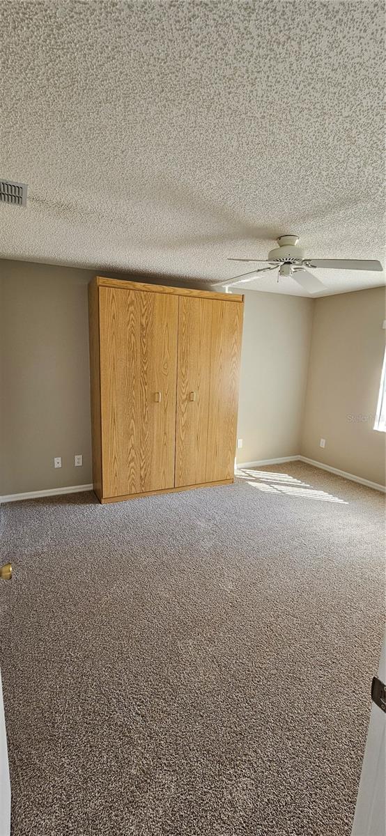 carpeted spare room with ceiling fan and a textured ceiling