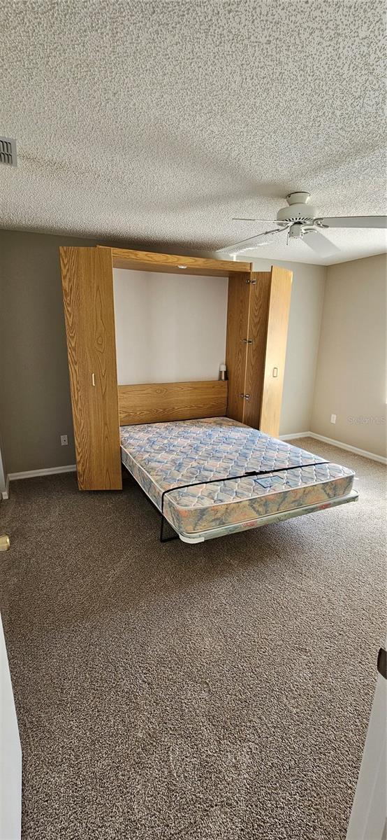 unfurnished bedroom featuring ceiling fan, a textured ceiling, and dark colored carpet