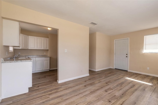 kitchen featuring sink, light hardwood / wood-style floors, white cabinets, and light stone countertops