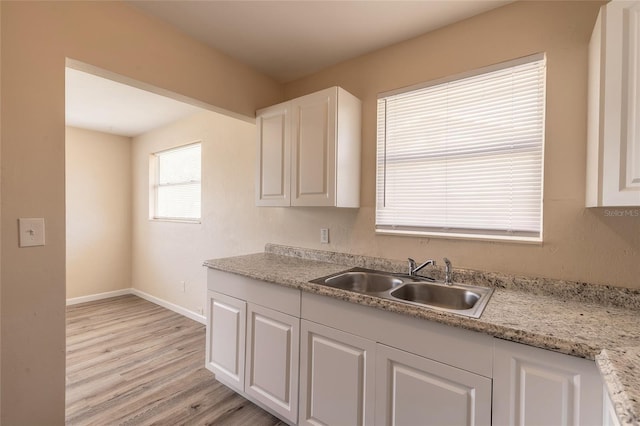 kitchen featuring sink, light stone countertops, white cabinets, and light wood-type flooring