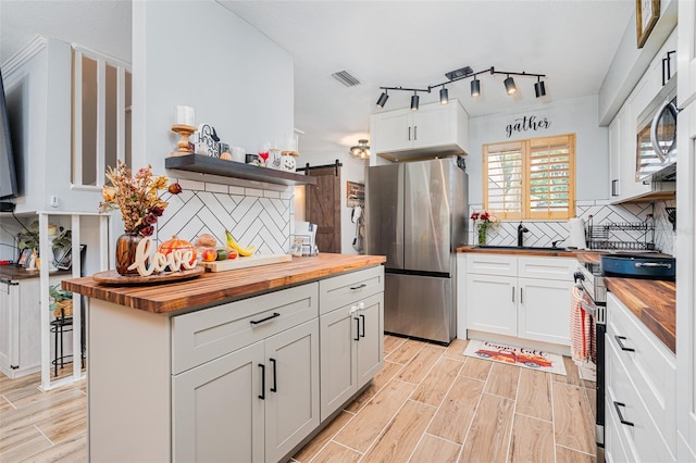 kitchen featuring appliances with stainless steel finishes, white cabinets, wooden counters, decorative backsplash, and a barn door