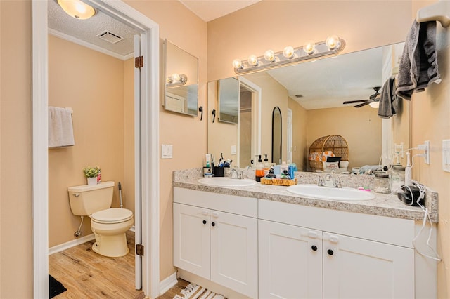 bathroom featuring wood-type flooring, ornamental molding, vanity, toilet, and a textured ceiling