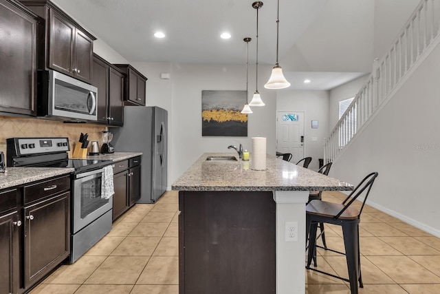 kitchen with appliances with stainless steel finishes, decorative light fixtures, a kitchen island with sink, a breakfast bar, and sink