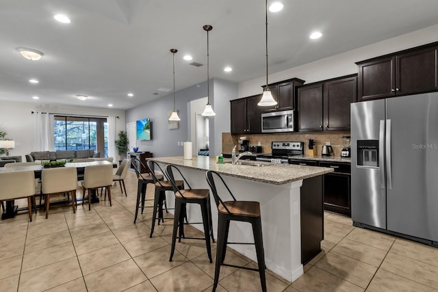 kitchen featuring pendant lighting, stainless steel appliances, light stone counters, a center island with sink, and a breakfast bar area