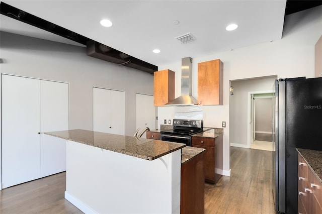 kitchen with appliances with stainless steel finishes, wall chimney exhaust hood, a kitchen island, light wood-type flooring, and a breakfast bar area