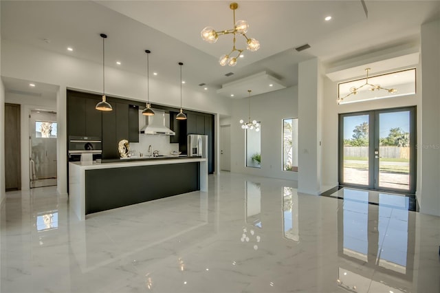 kitchen featuring decorative light fixtures, a kitchen island with sink, french doors, wall chimney range hood, and sink