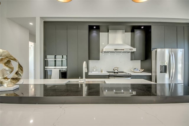 kitchen featuring wall chimney range hood, dark stone countertops, gray cabinets, decorative backsplash, and appliances with stainless steel finishes