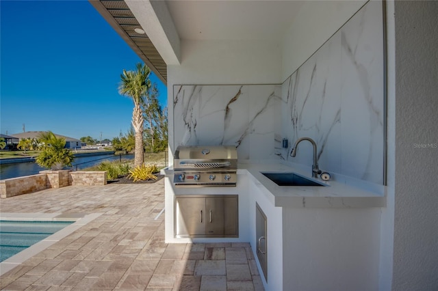 view of patio / terrace featuring a water view, exterior kitchen, sink, and a grill