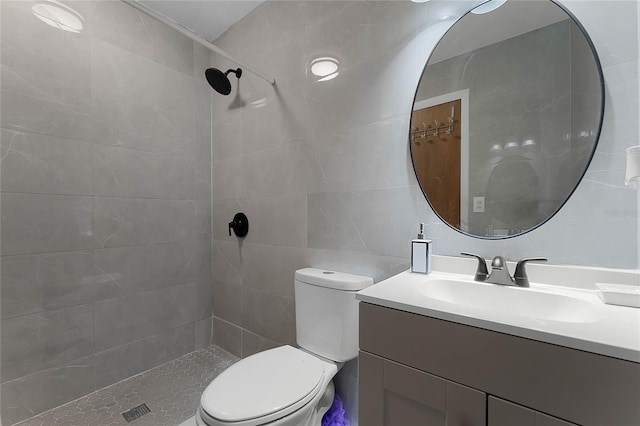 bathroom with vanity, tile walls, toilet, and tiled shower