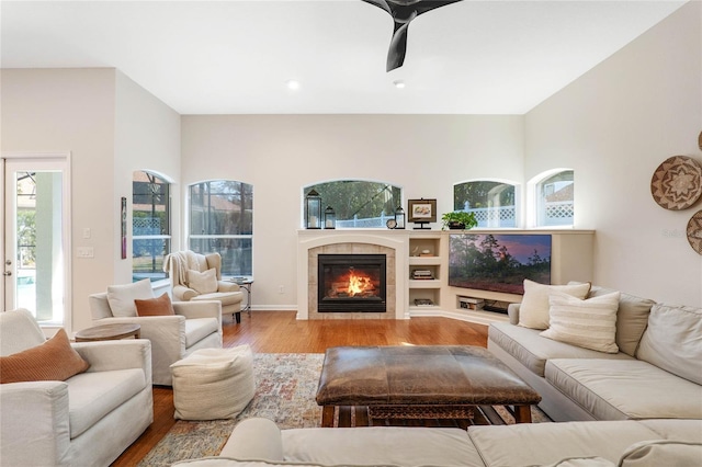 living room featuring light wood-type flooring, ceiling fan, a wealth of natural light, and a tiled fireplace